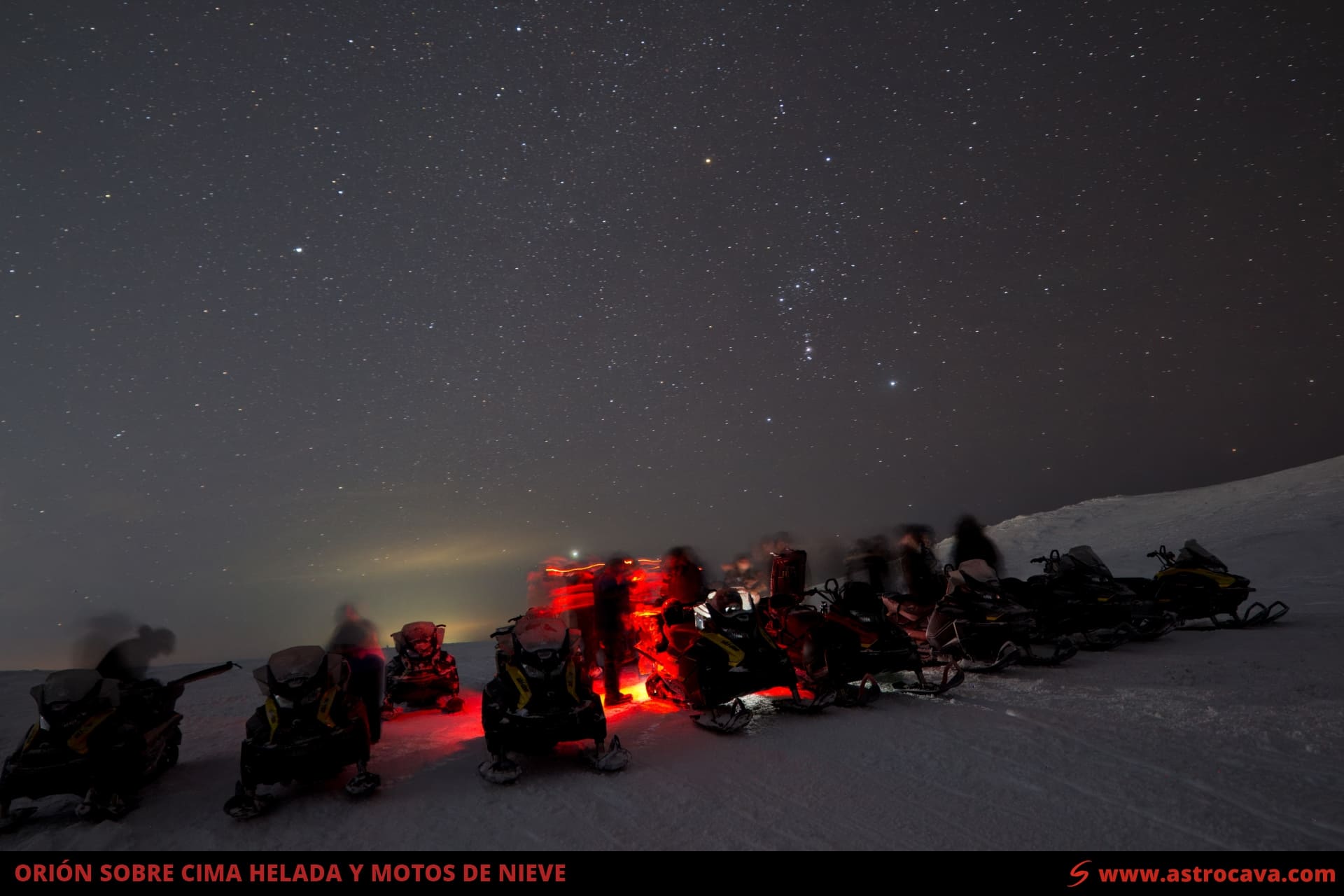 El cielo de invierno con la constelación de Orión sobre una cima helada y un grupo de motos de nieve.